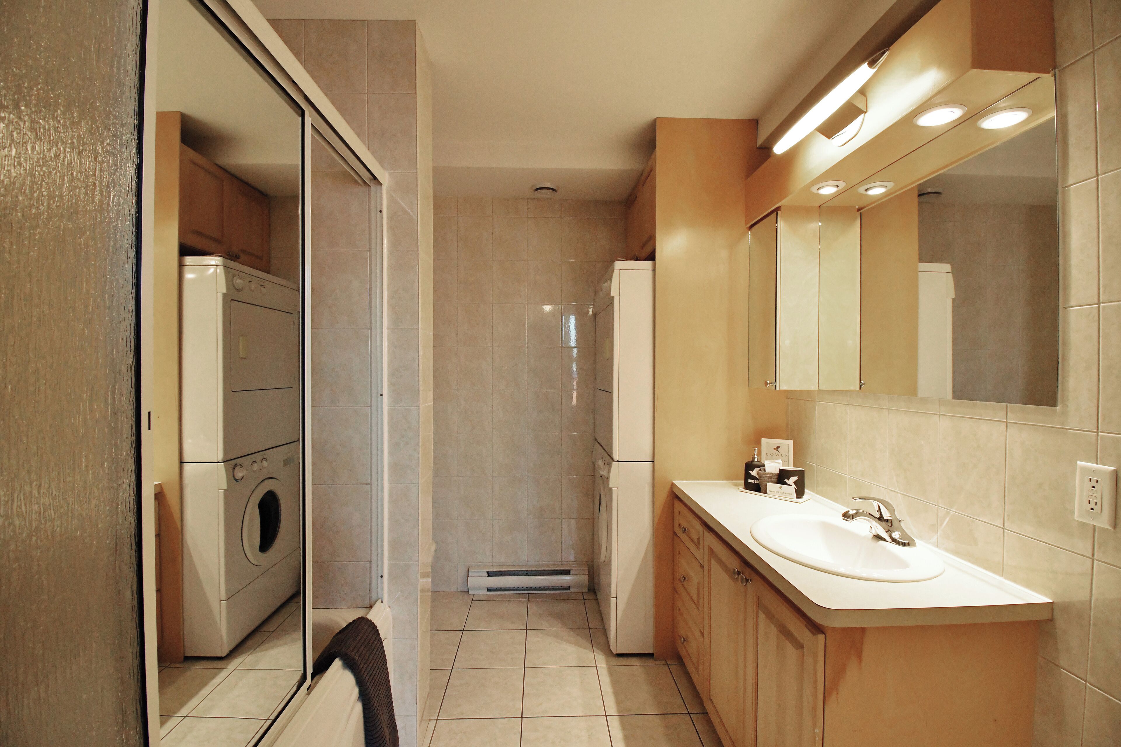 A modern bathroom with a built-in washer and dryer, a large mirror, and a vanity with a sink.