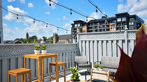 A rooftop terrace with wooden furniture, potted plants, and string lights. - Lester Lofts by Bower Boutique Hotels (Moncton)