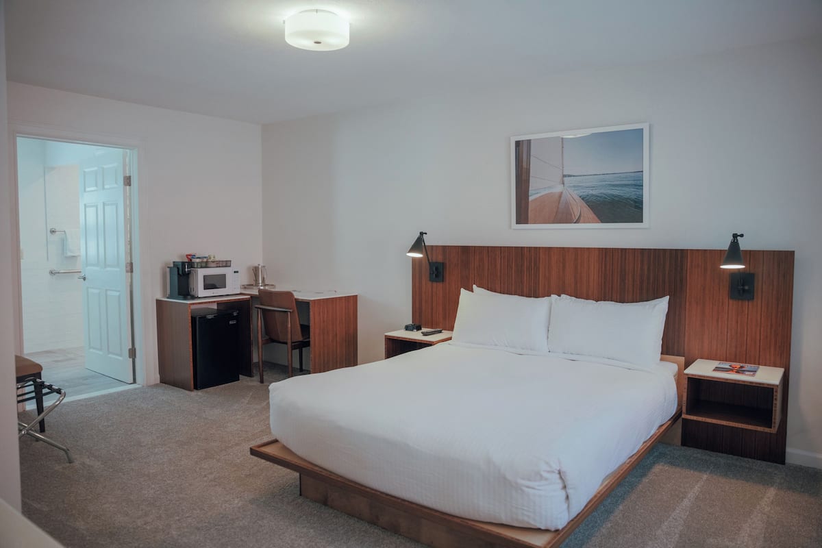 Een hotelkamer met een groot bed, een bureau met een magnetron, een stoel en een klein tafeltje.
