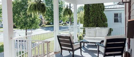 A covered porch with a white railing, two chairs, a small table, and a white sofa.