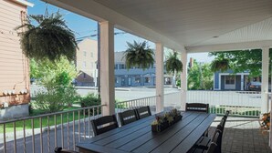 Eine überdachte Terrasse im Freien mit einem Holztisch und -stühlen, umgeben von einer weißen Brüstung.