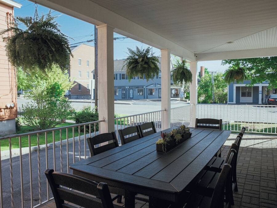 Un patio techado al aire libre con una mesa y sillas de madera, rodeado por una barandilla blanca.