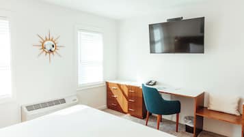 Une chambre à coucher avec un lit, un bureau avec une chaise, une télévision et un miroir décoratif en forme de soleil accroché au mur.