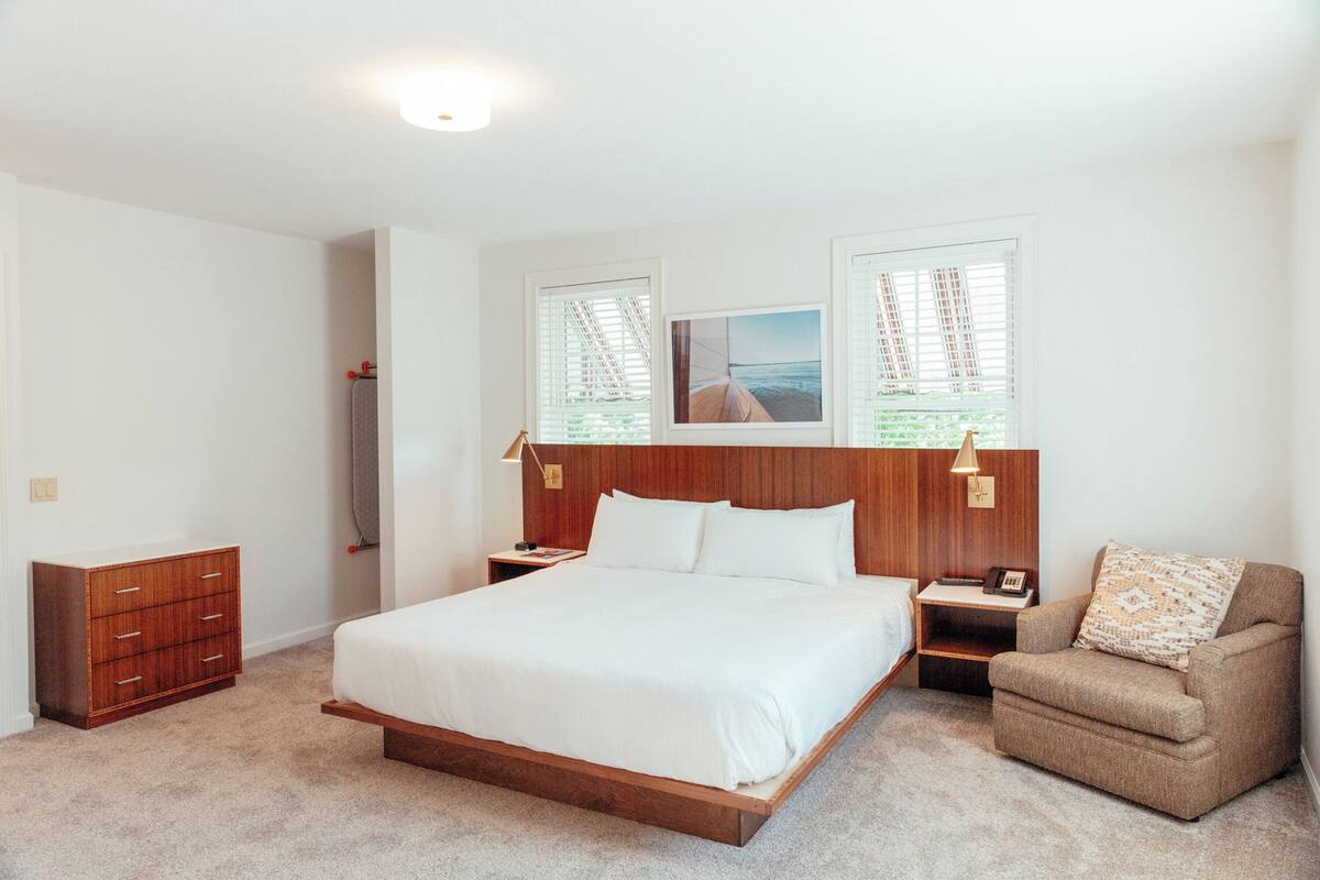 Een slaapkamer met een houten bed, twee nachtkastjes, een dressoir en een raam met jaloezieën.