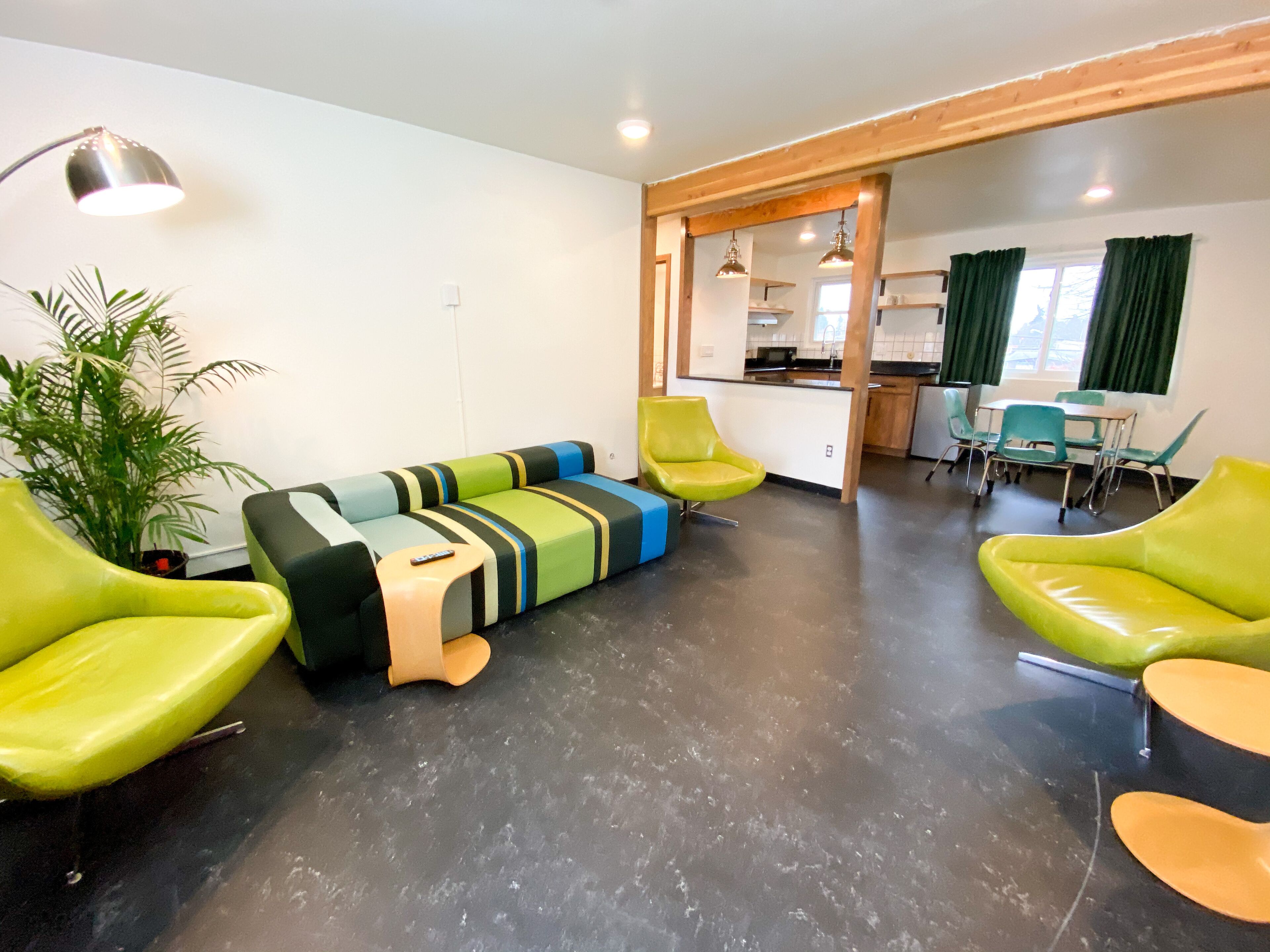 A modern living area with a sofa, chairs, a dining table, and a kitchen in the background.