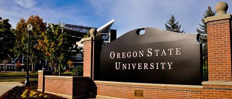 A sign for Oregon State University with a modern design, featuring a curved top and a brick base.