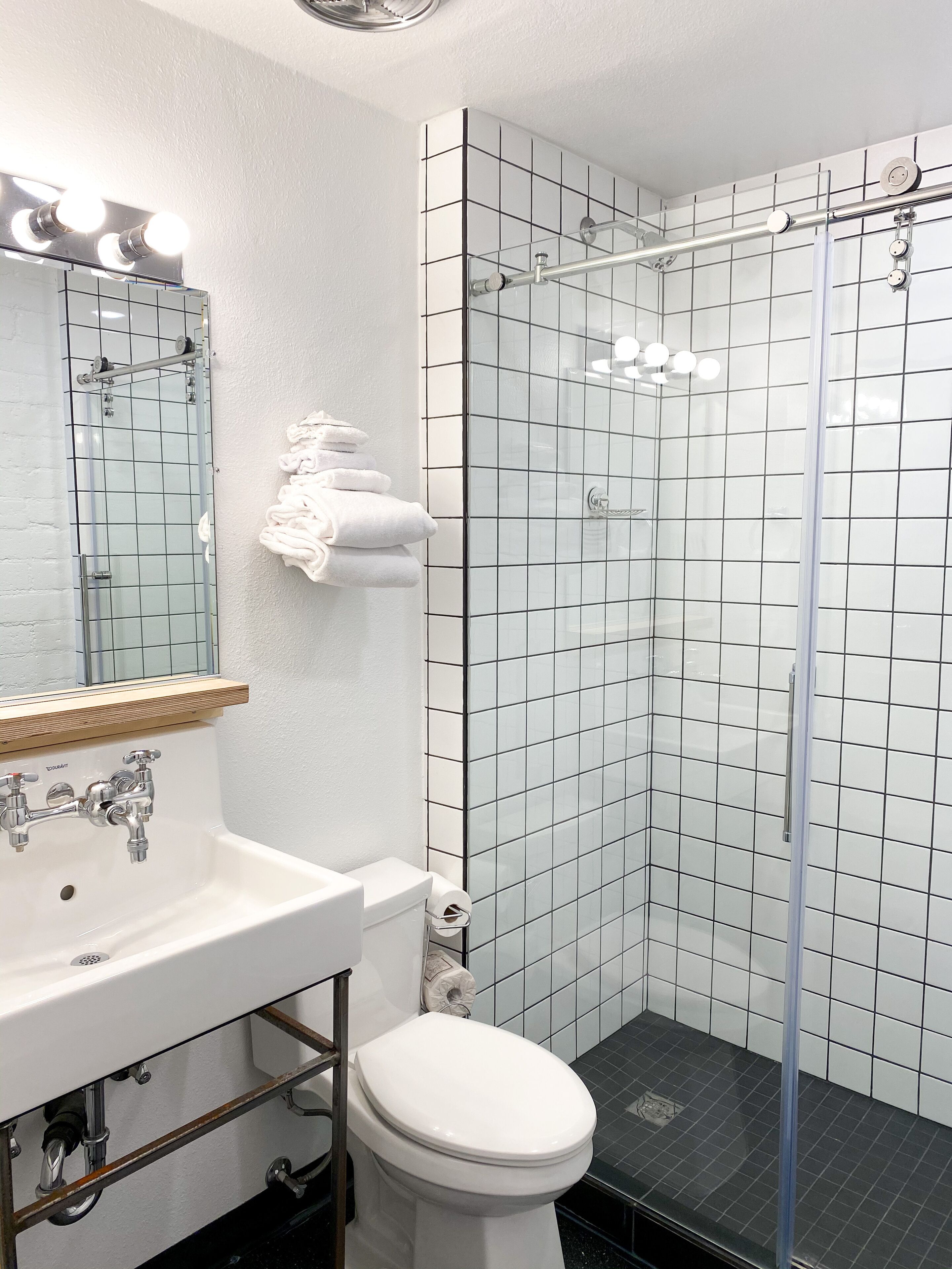 A modern bathroom with a white sink, mirror, and toilet. It includes a glass shower enclosure with a black floor.