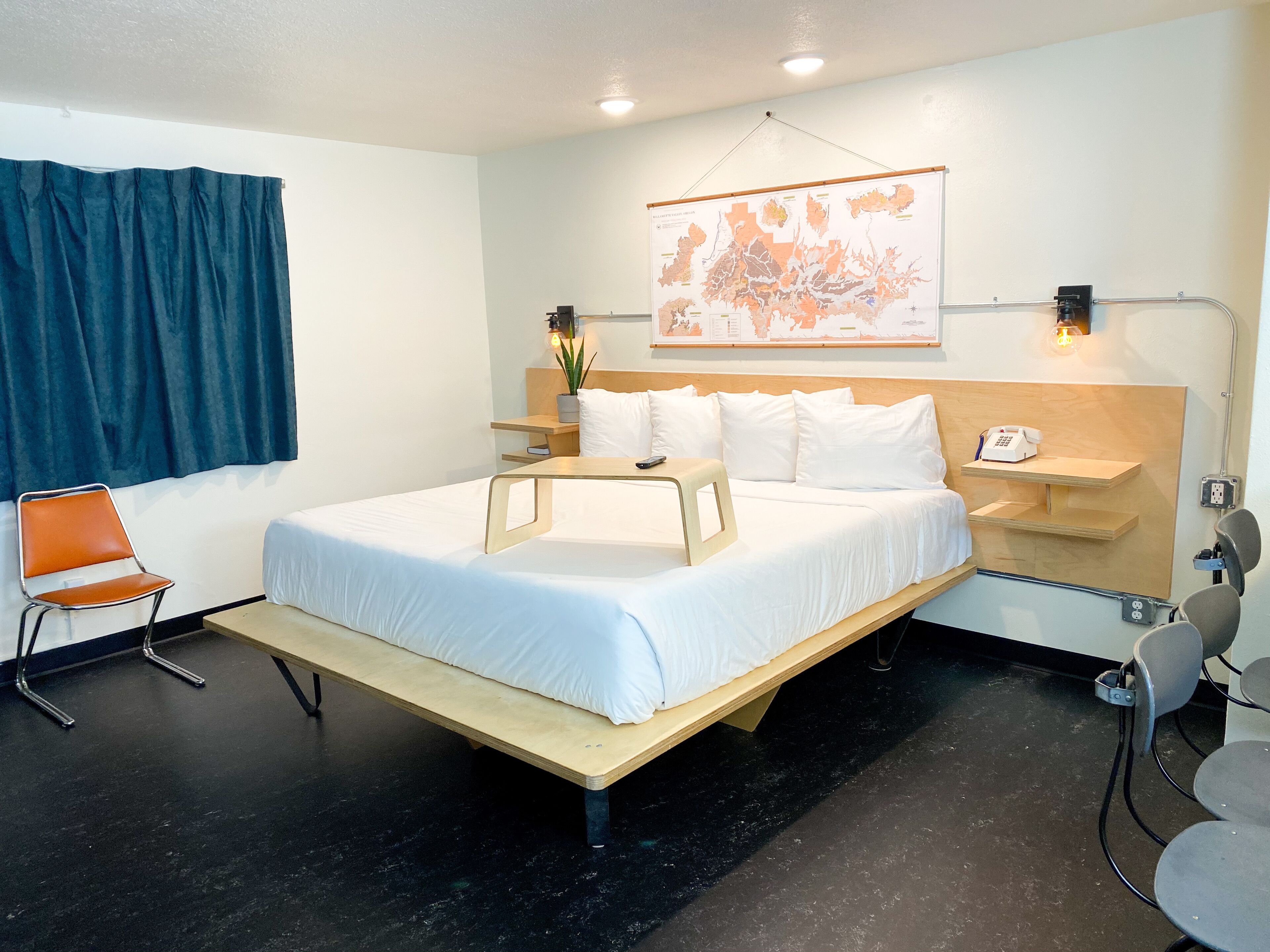 Ein modernes Hotelzimmer mit einem Bett, einem Schreibtisch, einem Stuhl, einer Karte an der Wand und einem blauen Vorhang.