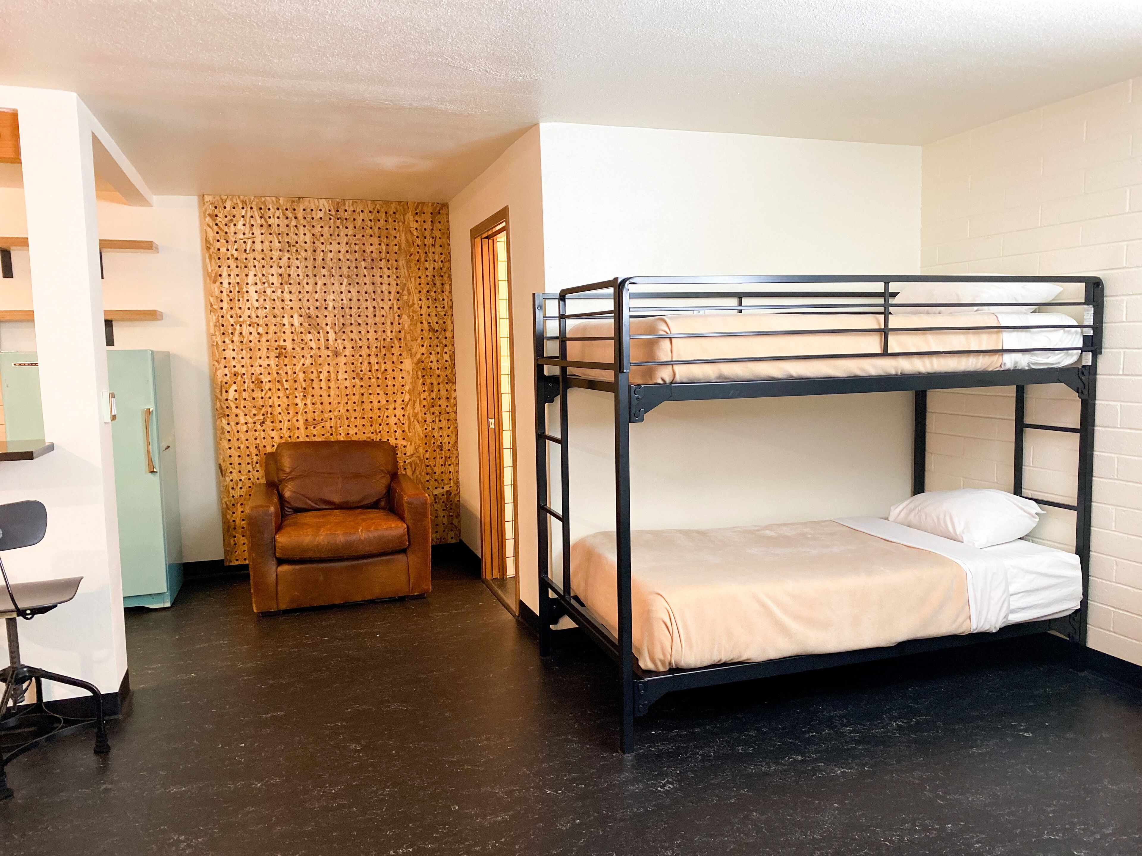 A bunk bed with a chair and a desk in a room with patterned wallpaper and a light-colored floor.