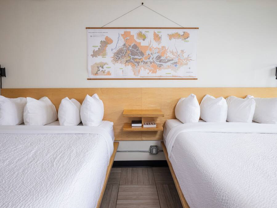 Une chambre d’hôtel avec deux lits, une tête de lit en bois, une carte accrochée au mur et une petite table sur laquelle se trouvent un livre et une lampe.