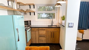 A compact kitchen with wooden cabinets, a vintage teal refrigerator, a microwave, and a window with blinds.