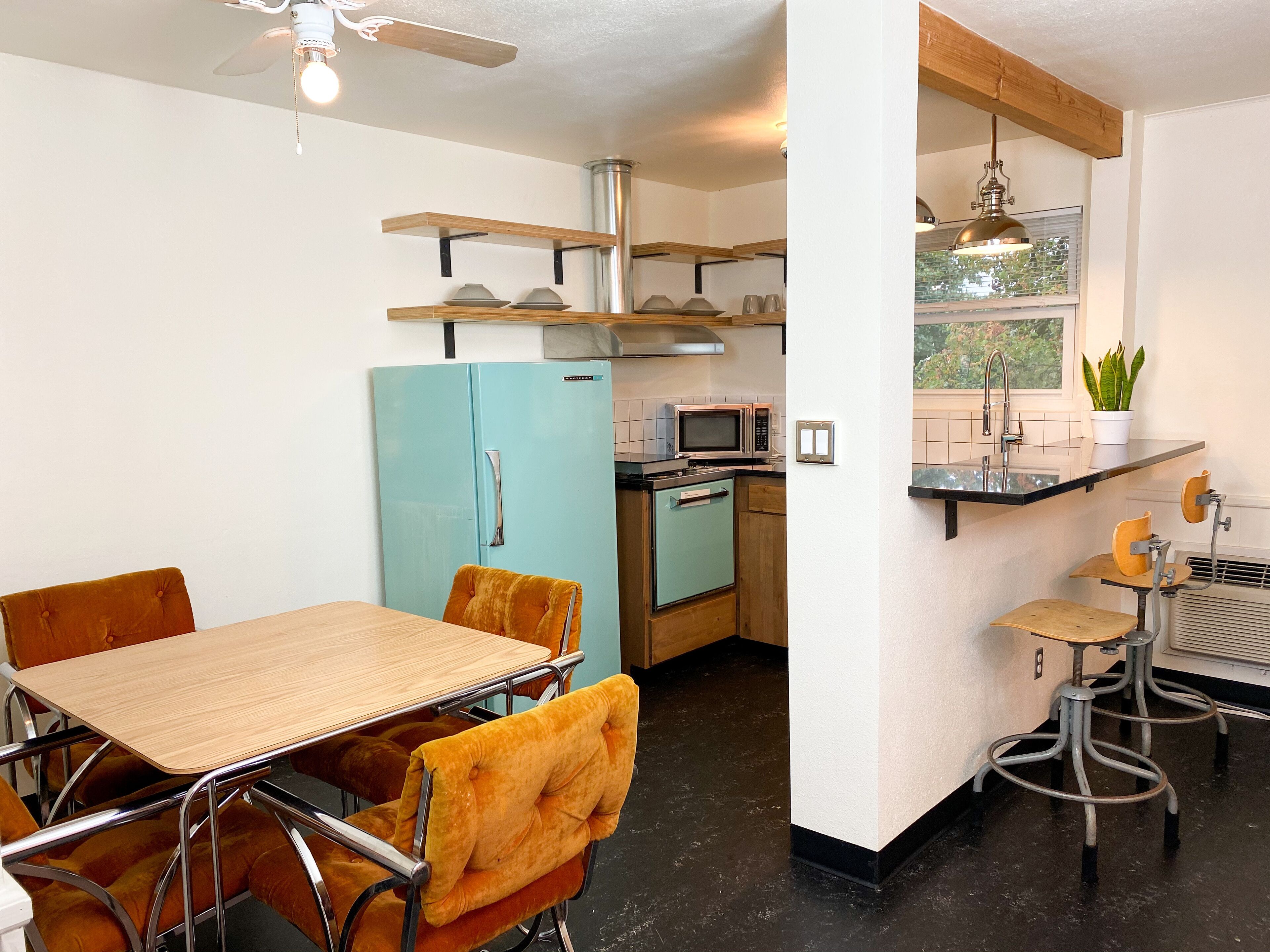 A compact kitchen with a blue refrigerator, a microwave, and a sink. There is a dining area with a wooden table and orange chairs.