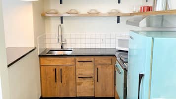 Une cuisine avec des meubles de rangement en bois, un plan de travail noir, un évier, une cuisinière et un réfrigérateur bleu.