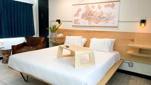 A hotel room with a large bed, a desk, a chair, a map on the wall, and a potted plant.