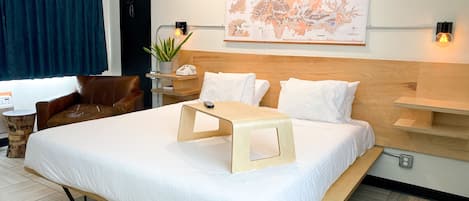 A hotel room with a large bed, a desk, a chair, a map on the wall, and a potted plant.