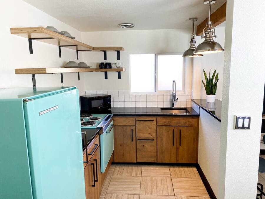 Una cocina compacta con un refrigerador verde azulado, armarios de madera, un microondas y una estufa.