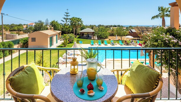 A balcony with a view of a swimming pool, outdoor seating, and a gazebo.