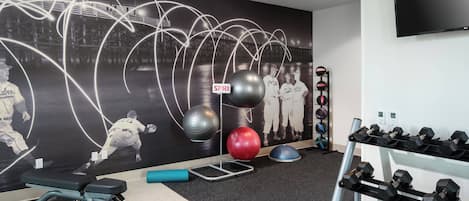 A gym with exercise equipment, a wall mural, and a TV mounted on the wall.