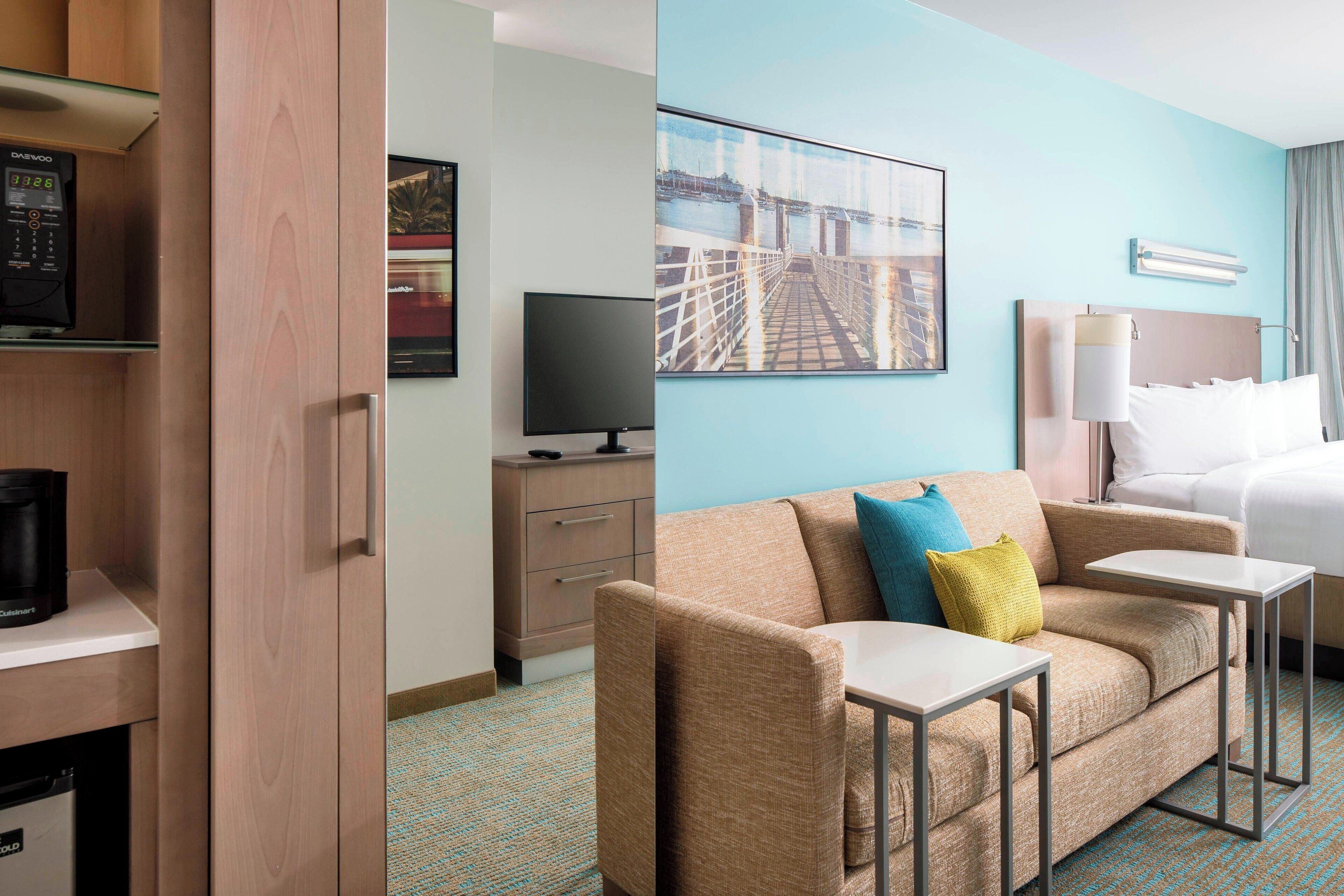 A hotel room with a sofa, a small table, a TV, a coffee machine, and a bed.