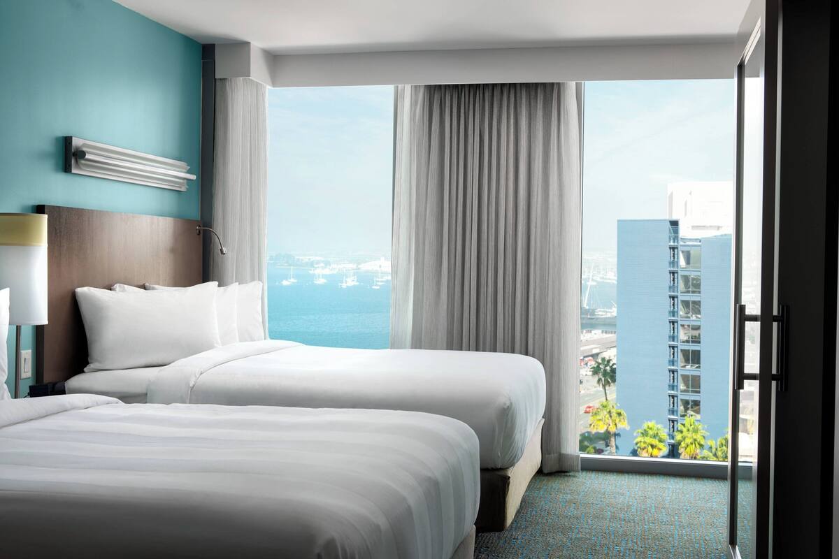 A hotel room with two beds, a view of the city, and a large window with curtains.