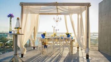 An outdoor wedding setup with a white canopy, a tiered cake, and a view of the sea.