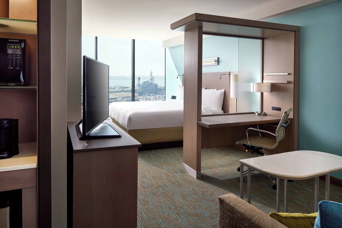 A hotel room with a bed, desk, chair, and a view of the city.