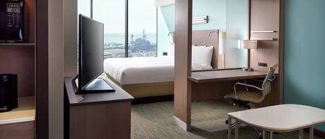 A hotel room with a bed, desk, chair, and a view of the city.