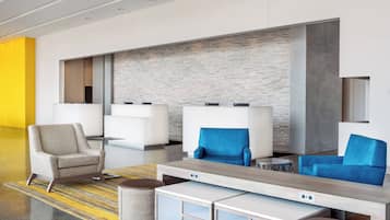 Eine moderne Lobby mit einer Rezeption, zwei Sitzbereichen mit blauen und beigen Stühlen, einem gemusterten Teppich und einer Wand aus Ziegelsteinen.