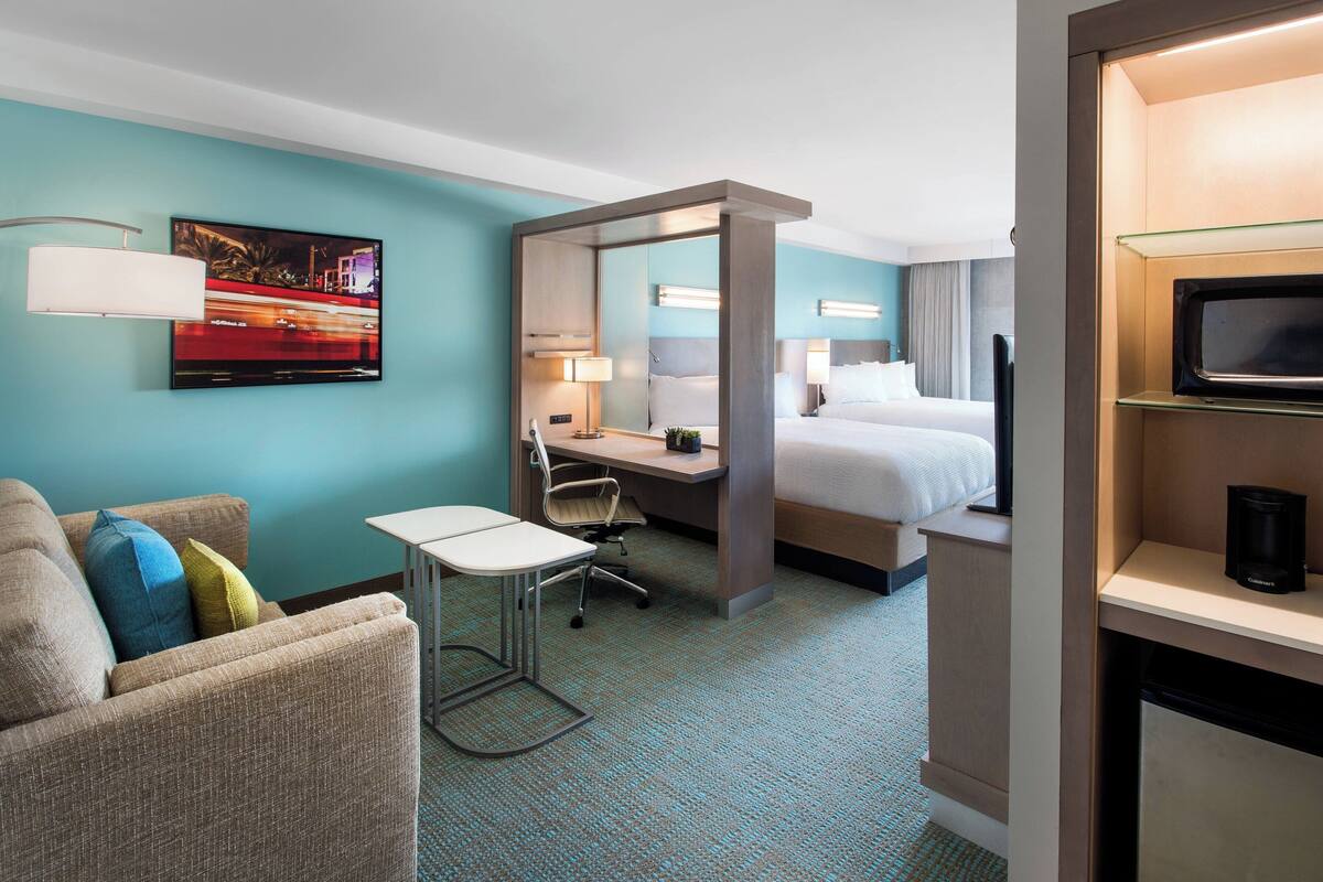 A hotel room with a bed, a desk with a chair, a television, and a large window.