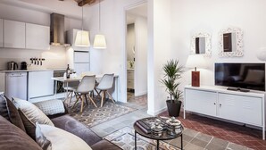 A modern living room with a sofa, a coffee table, a TV, and a dining area with chairs and a table. - Aspasios Charming Flats (Barcelona)
