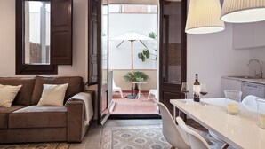 A cozy living room with a brown sofa, a dining table, and a kitchen area with a sink and cabinets. - Aspasios Charming Flats (Barcelona)