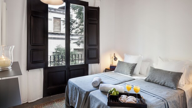 A bedroom with a bed, bedside table, and a tray with food and drinks. - Aspasios Charming Flats (Barcelona)