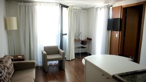 Ett hotellrum med en soffa, en fåtölj, ett skrivbord, en tv och ett litet kök.