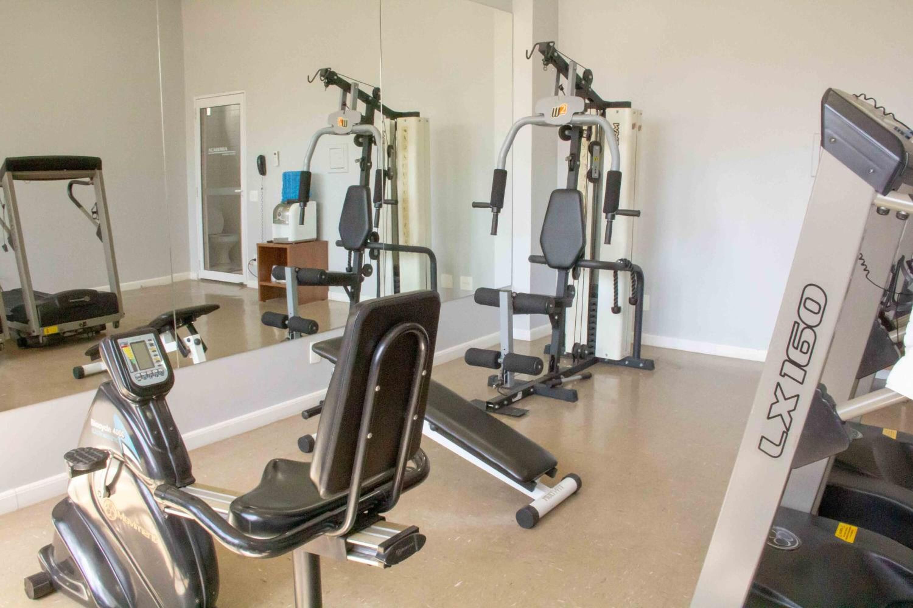 Ett gym med konditionsmaskiner, styrketräningsmaskiner och en vägg med speglar.
