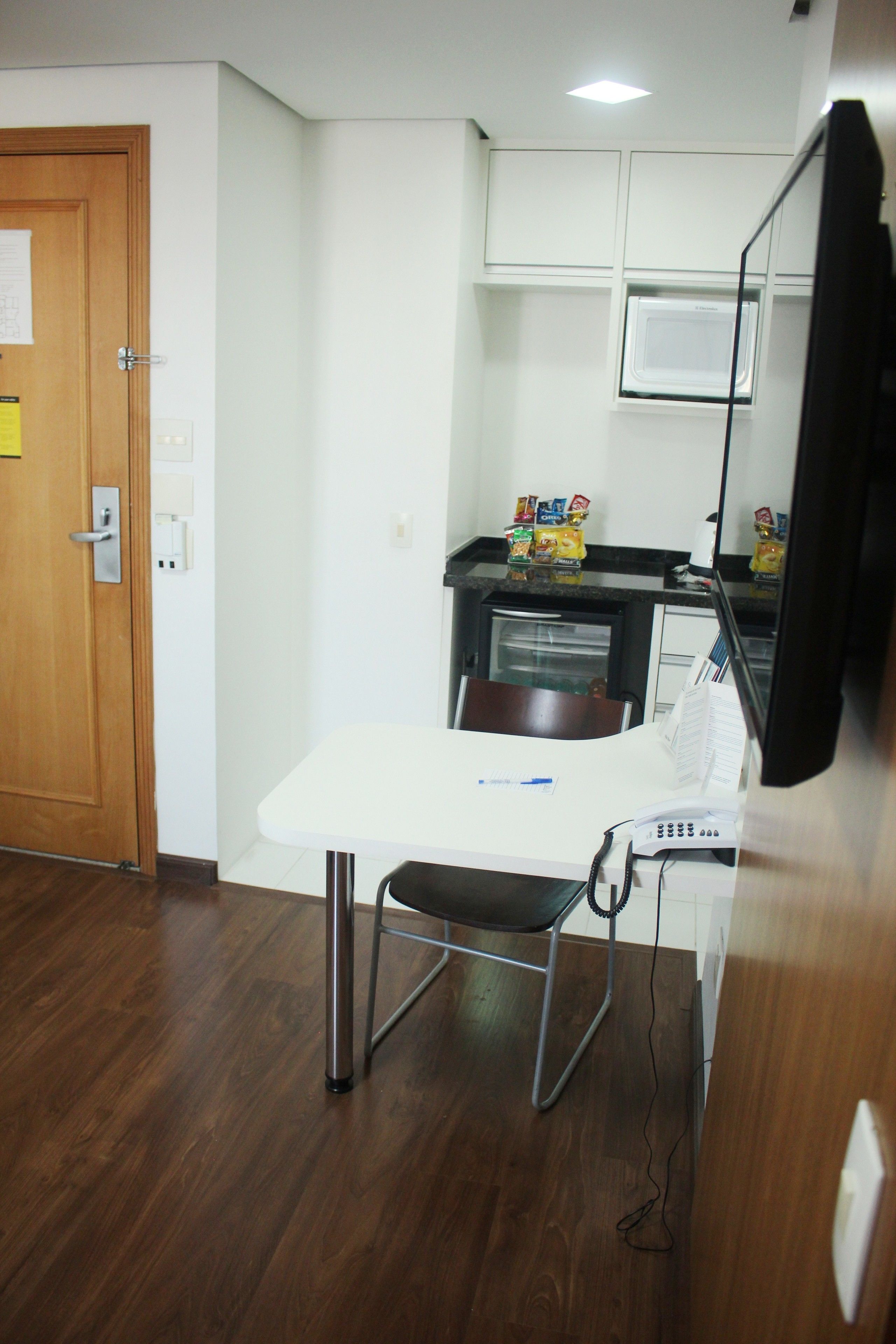 A small kitchenette with a microwave, a refrigerator, and a countertop with snacks.