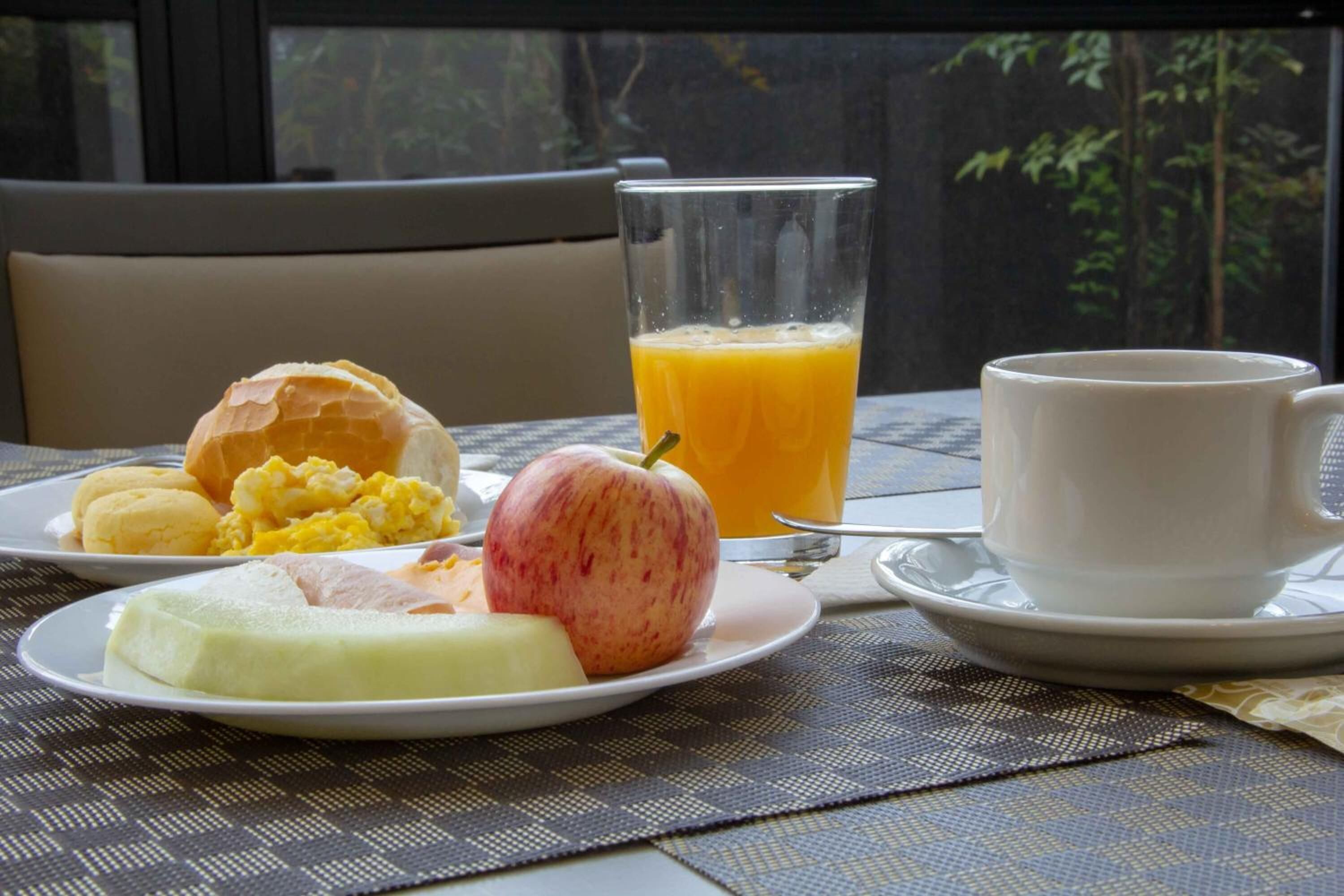 Mesa posta para o café da manhã, com um prato de comida, um copo de suco de laranja e uma xícara.