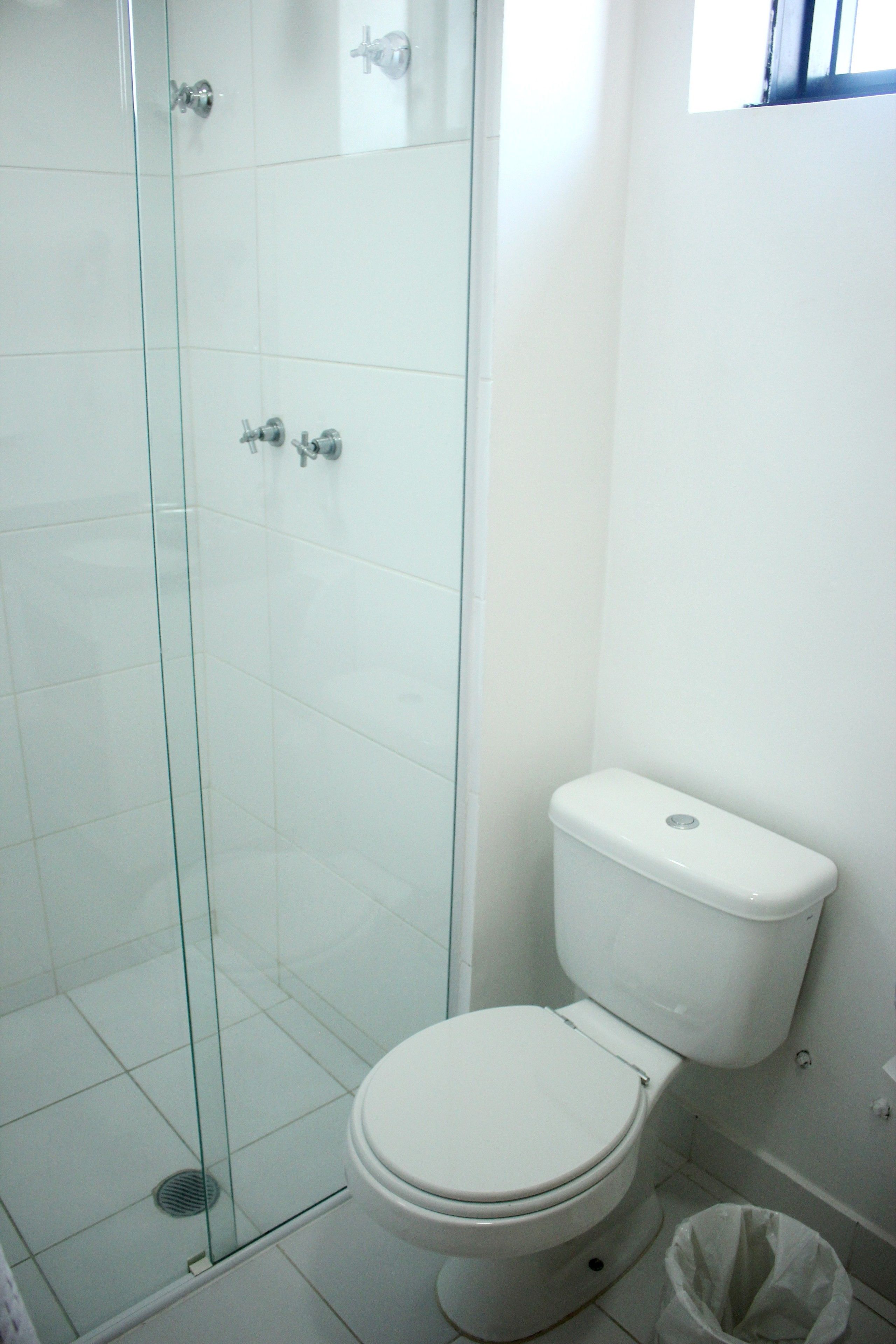 Un baño con cabina de ducha de vidrio, un inodoro blanco y un cubo de basura.