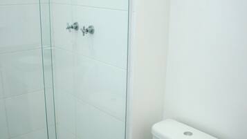 Un baño con cabina de ducha de vidrio, un inodoro blanco y un cubo de basura.