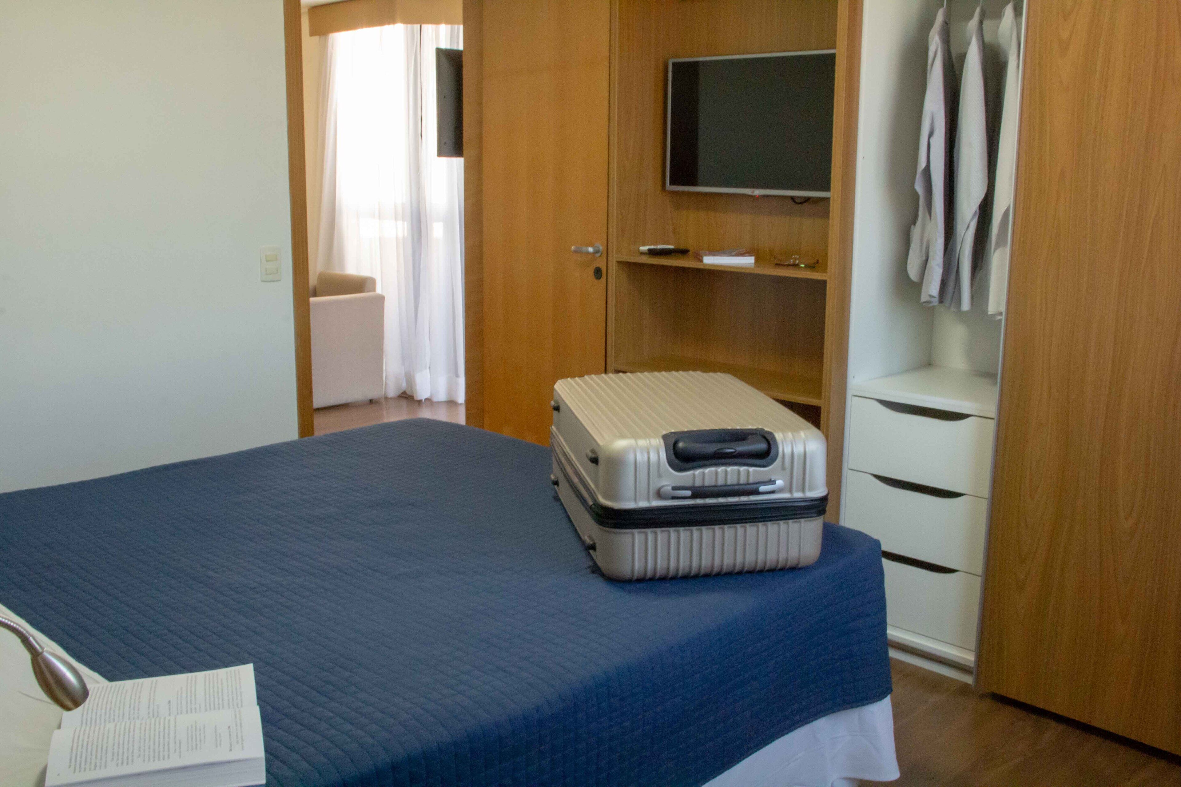 Ein Hotelzimmer mit einem Bett, einem Koffer, einem Fernseher auf einem Regal und einem Kleiderschrank.
