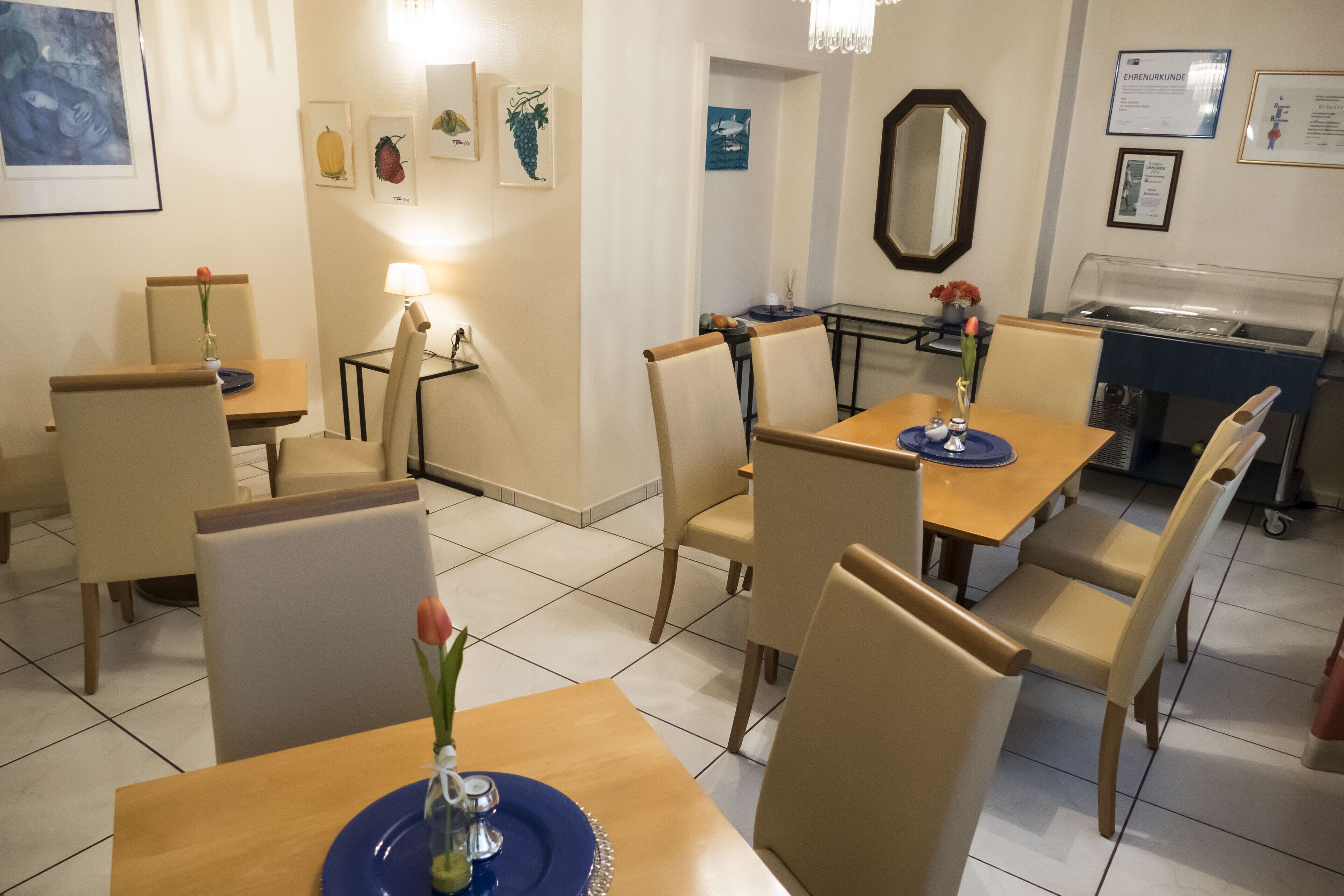Uma sala de jantar com várias mesas e cadeiras, um espaço para buffet e obras de arte nas paredes.