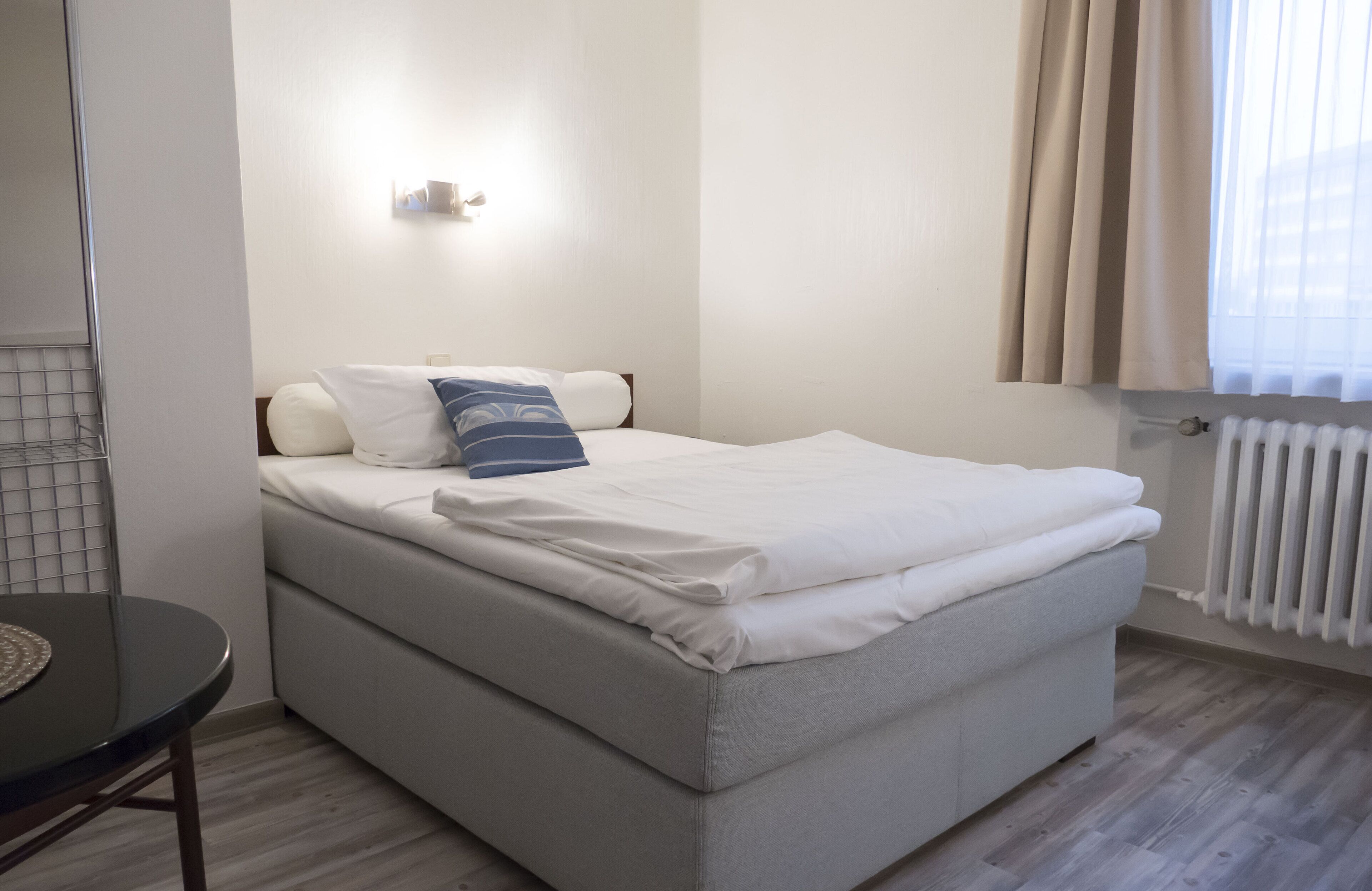 Una cama individual con ropa blanca, una mesita de noche y una ventana con cortinas.