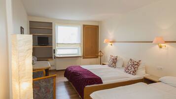A hotel room with two beds, a desk, a chair, a TV, and a window.