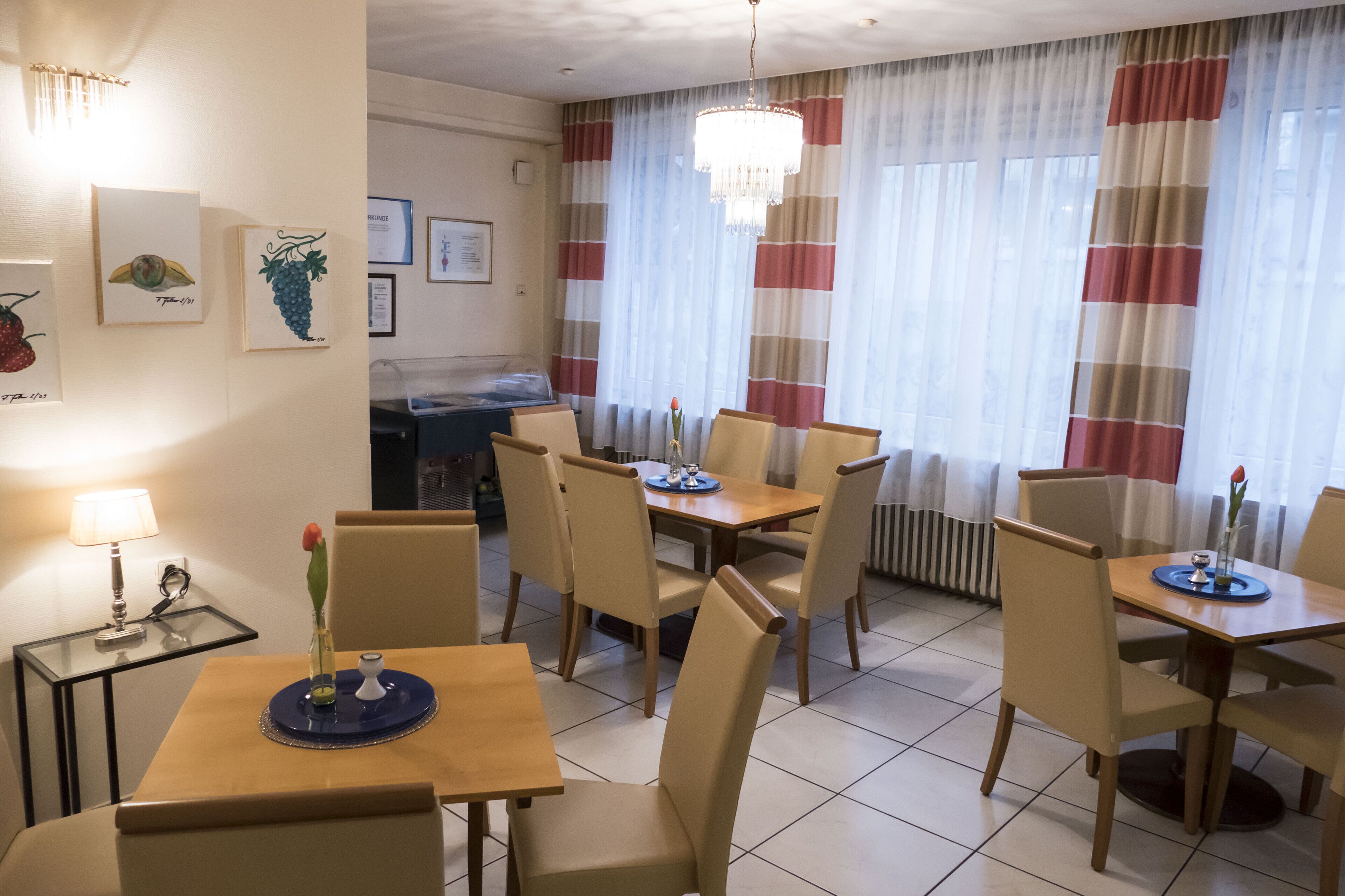 Comedor de hotel con varias mesas y sillas, un candelabro y obras de arte en las paredes.