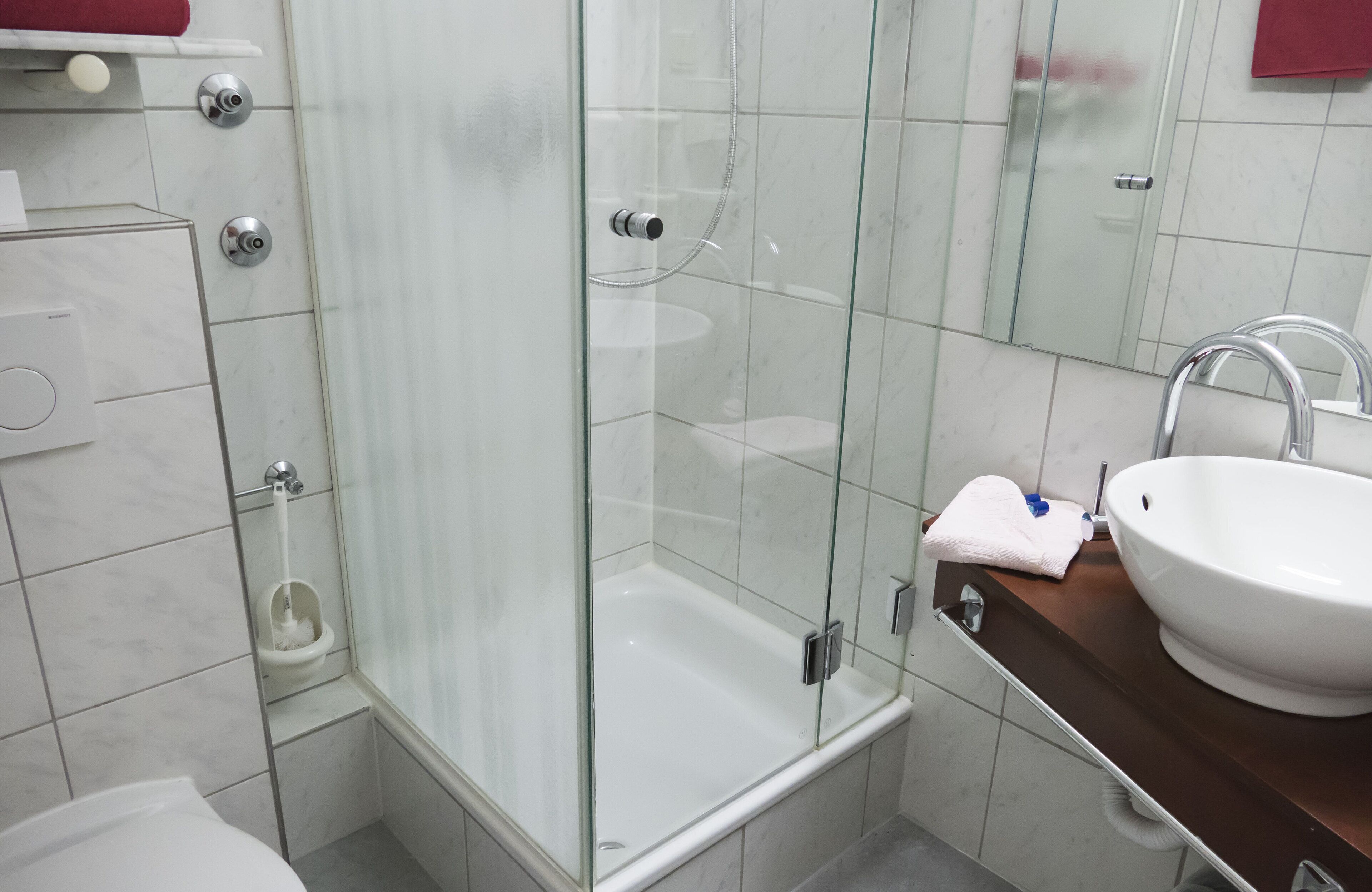 A modern bathroom with a glass-enclosed shower, a white sink, and a marble-tiled wall.
