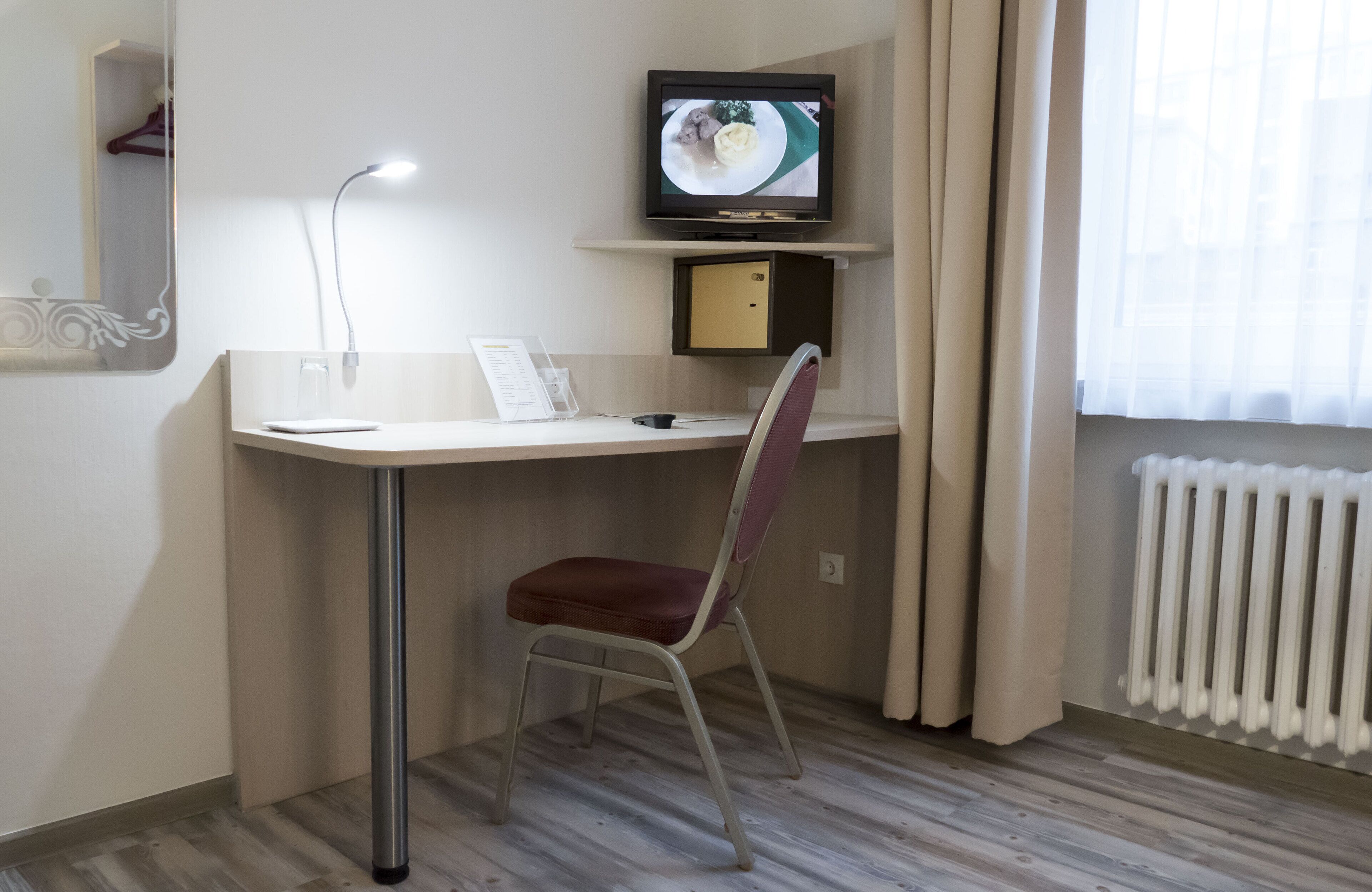 Una habitación pequeña y moderna con escritorio, silla, televisor y radiador.