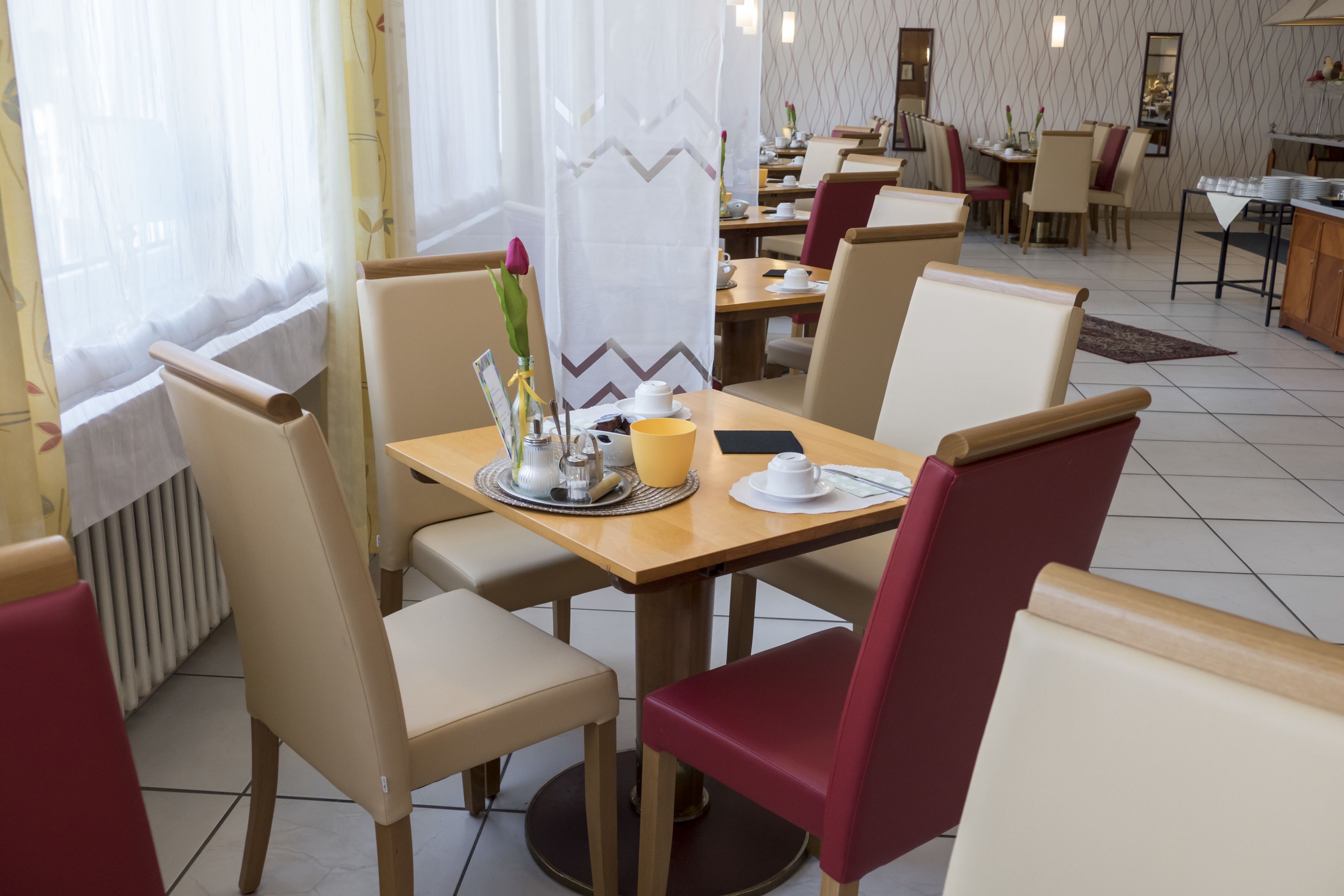 Un restaurante con una mesa dispuesta para dos, que incluye un florero con flores, una taza amarilla y una taza blanca.