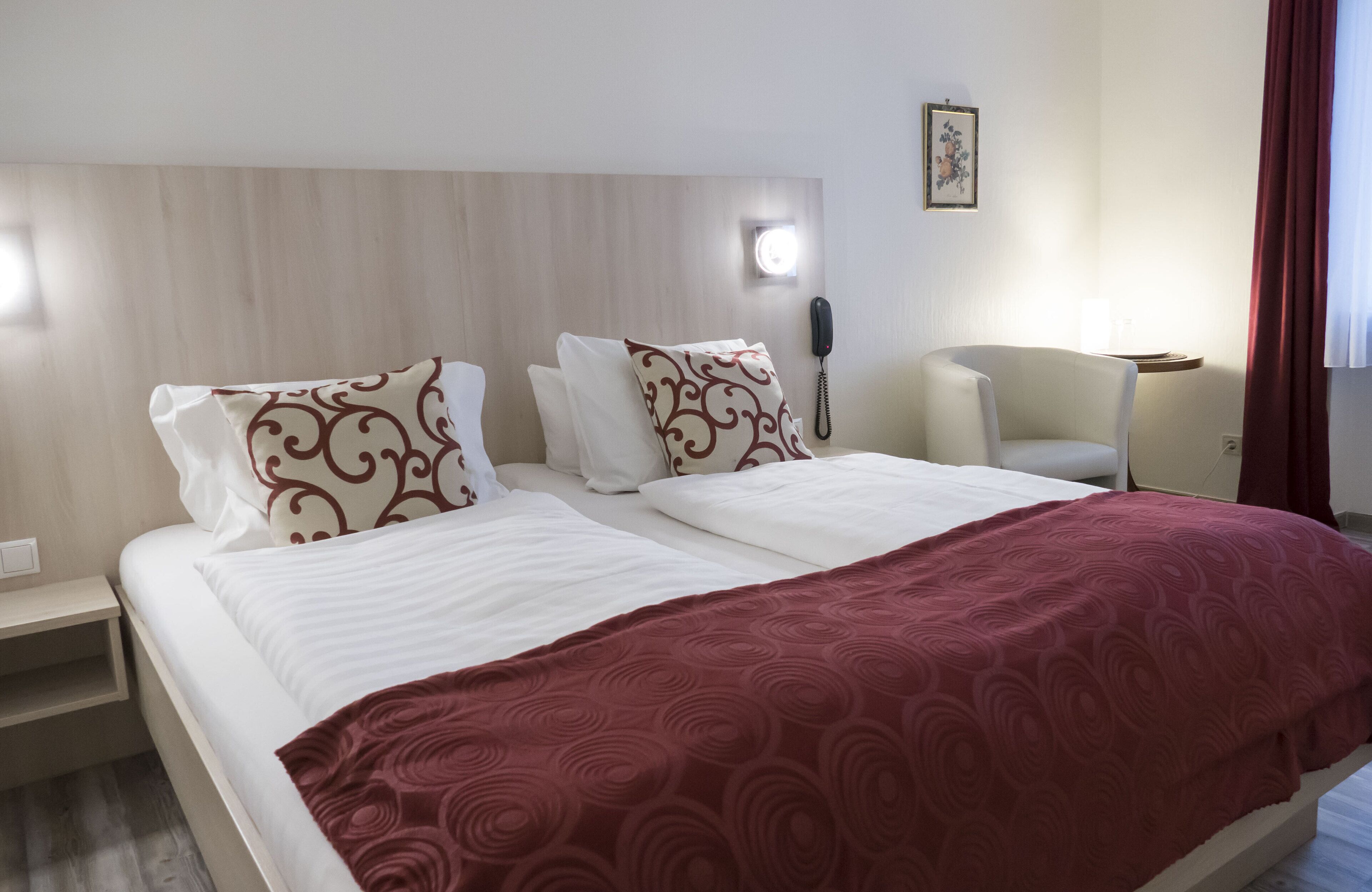 A hotel room with a bed, a bedside table, a chair, a phone, and a wall-mounted light.