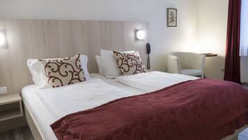 A hotel room with a bed, a bedside table, a chair, a phone, and a wall-mounted light.