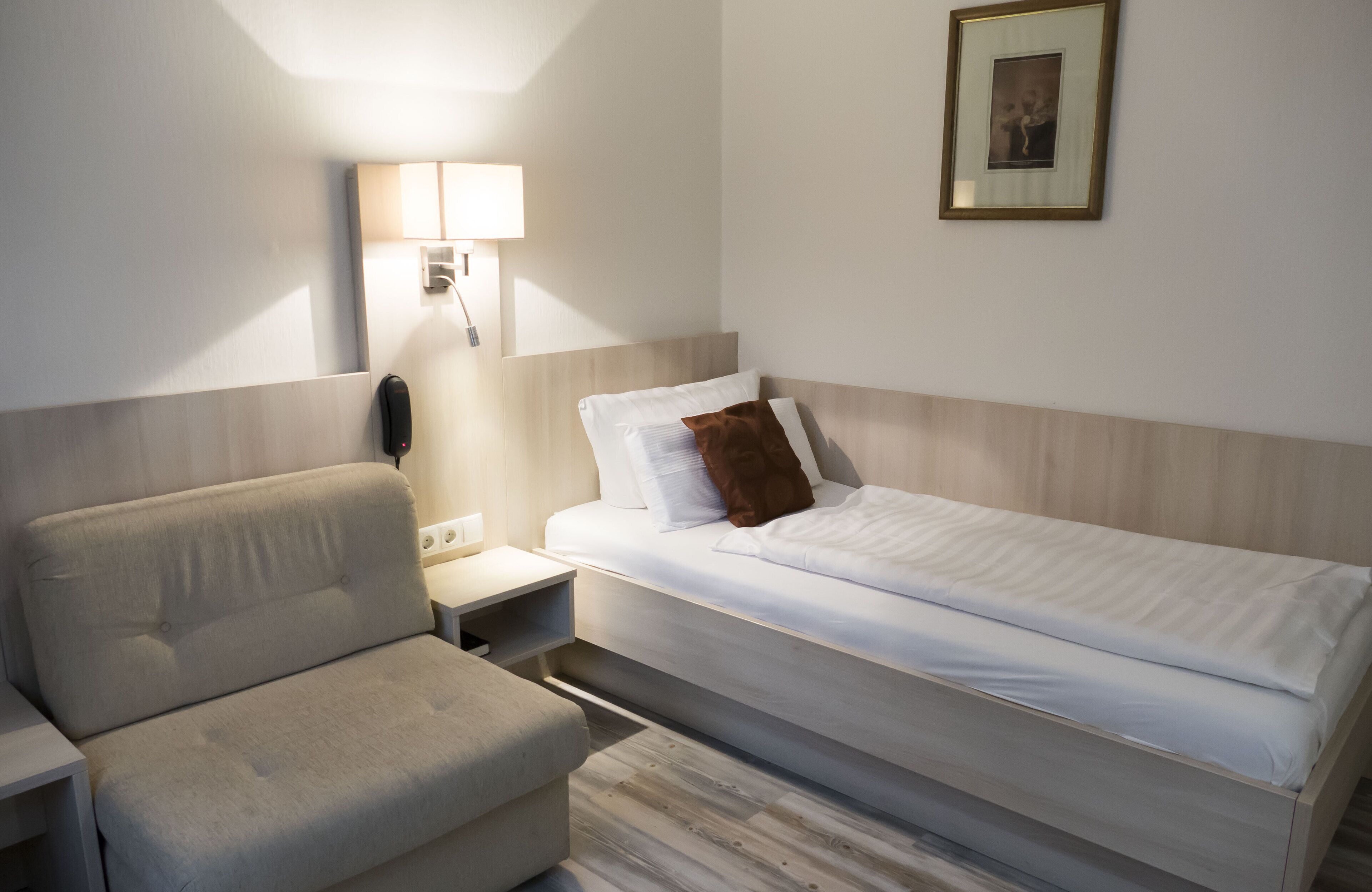 A hotel room with a single bed, a bedside table, a lamp, and a chair.