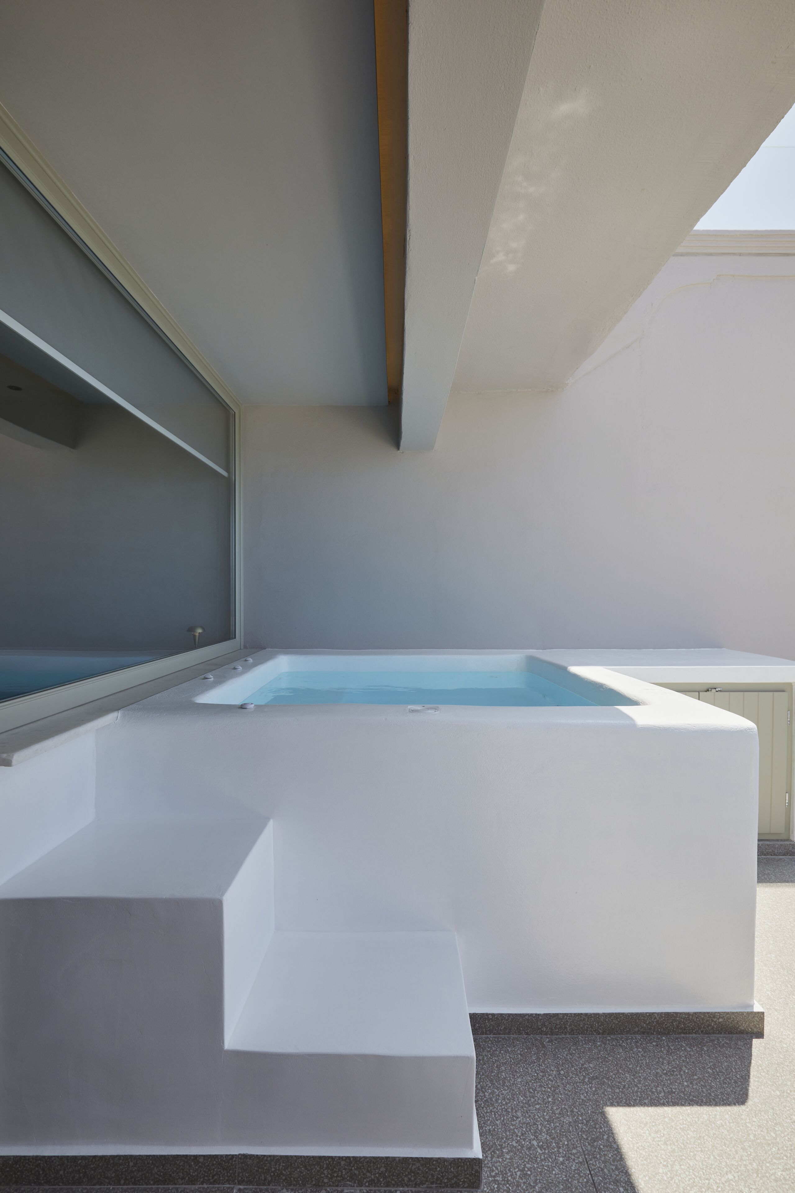 A modern outdoor pool area with a rectangular pool, a built-in bench, and a glass enclosure.